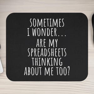 May include: Black rectangular mousepad with the text "SOMETIMES I WONDER... ARE MY SPREADSHEETS THINKING ABOUT ME TOO?" in white. A black computer mouse and part of a keyboard are visible.
