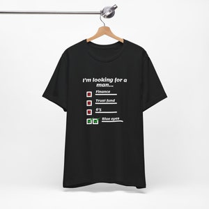 May include: Black t-shirt with the text "I'm looking for a man..." and a checklist. The checklist includes "Finance", "Trust fund", "6'5", and "Blue eyes", with only "Blue eyes" checked.