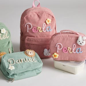 Peut inclure: Ensemble de sacs à dos, sacs à déjeuner et trousses en velours côtelé pastel. Chaque article présente des noms brodés et des appliqués décoratifs tels que des fleurs, un lion et un lapin. Articles pour enfants.
