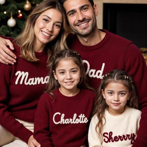 May include: A family of four wearing matching burgundy sweaters with white text. The sweaters read "Mama", "Dad", "Charlotte", and "Sherry". The family is smiling in front of a Christmas tree.