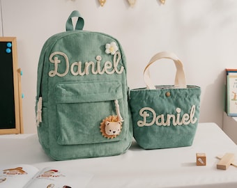 May include: A mint green corduroy backpack and matching tote bag. The backpack features the name "Daniel" in a cream-colored script, a small flower, and a lion applique. The tote bag also has "Daniel" in the same script.