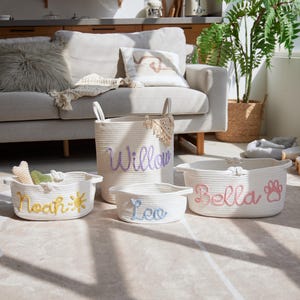 Puede incluir: Conjunto de cestas de cuerda blancas con nombres bordados: "Willow" en morado, "Noah" con un sol amarillo, "Leo" en azul y "Bella" con una huella rosa. Cestas de diferentes tama&ntilde;os para accesorios de mascotas.