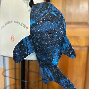 Może przedstawiać: Niebieska i czarna torba na ramię w kształcie rekina wielorybiego z złotymi akcentami brokatowymi. Torba ma regulowany czarny pasek.