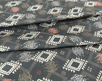 May include: Dark gray fabric with a repeating geometric pattern. White, brown, and coral-colored diamond and geometric shapes are scattered across the fabric. The fabric is folded, showing texture and depth.