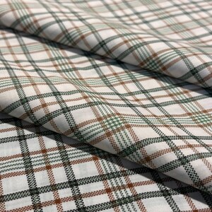 May include: Close-up of a white fabric with a plaid pattern in shades of green and brown. The fabric is folded, showing the texture and the arrangement of the plaid design. The pattern is a classic, timeless design.