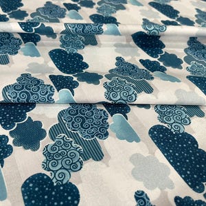May include: White fabric with a repeating pattern of stylized blue clouds. The clouds vary in design, some with polka dots, others with swirls, and some with striped accents. The fabric is folded, showing the pattern's continuity.