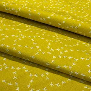 May include: Close-up of a folded fabric with a repeating pattern of white bird footprints on a yellow-green background. The fabric has a soft texture and a slight sheen, with the pattern creating a sense of movement.