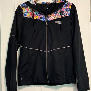 May include: Black hooded jacket with a colorful paint splatter design on the hood and a white "Volcom" logo on the front.