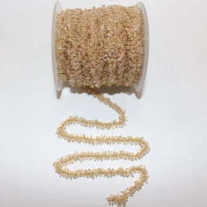 May include: A spool of gold-toned chain with clear faceted beads. The chain is made of small, delicate beads that are strung together in a continuous pattern.