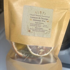 May include: A clear bag filled with dried lemon and orange slices, cloves, and rosemary. The bag has a label that reads "Chasin' Dreams Farmstead Lemon & Orange Simmer Pot." The ingredients and directions are also listed on the label.