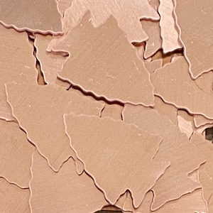 May include: A pile of rose gold metallic confetti shaped like Christmas trees. The confetti is scattered and overlapping.