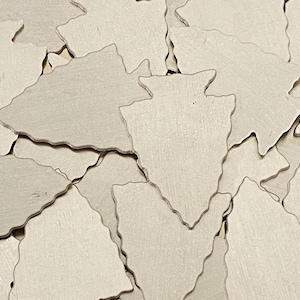 May include: A pile of light brown wooden arrowhead shapes. The arrowheads are all the same size and shape, and they are arranged in a random pattern.