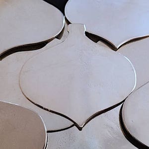 May include: A set of silver metal ornament shapes, each in the shape of a teardrop with a pointed tip. The ornaments are stacked on top of each other.