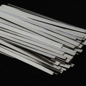 May include: A stack of thin, silver-colored metal strips. The strips are arranged in a neat pile, with the ends of the strips aligned.