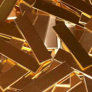 May include: A pile of gold-colored metal strips, stacked and overlapping. The strips are rectangular and have a smooth, shiny surface.