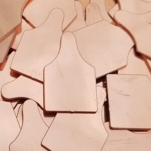 May include: A pile of small, light pink, metal tags with a rounded top and a pointed bottom. The tags are made of a thin metal and have a smooth, polished finish.