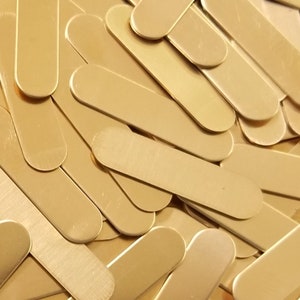 May include: A pile of gold-colored metal blanks, each shaped like a long oval. The blanks are smooth and have a slightly brushed finish.