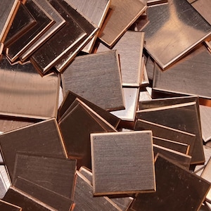 May include: A close-up shot of a pile of small, square copper metal pieces. The squares have a brushed finish and a warm, reddish-brown color. The edges of the squares are slightly raised, creating a subtle border. The pieces are scattered, overlapping each other.