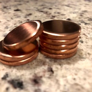 May include: Close-up of several copper-colored metal discs. Some discs are stacked, while others are scattered. The discs have a shiny, reflective surface. The image is well-lit, highlighting the metallic sheen of the objects.