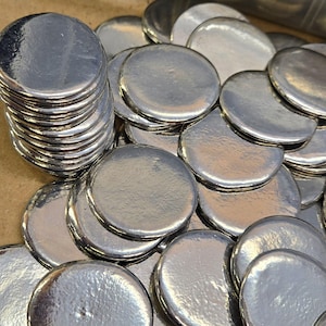 May include: A large pile of round, silver-colored metal discs. The discs are smooth and shiny, and they are stacked on top of each other.