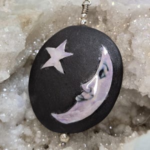 May include: A black ceramic pendant with a white crescent moon and a white five-pointed star. The pendant is on a silver chain.