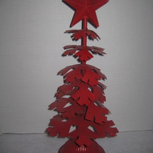 May include: A red metal Christmas tree with a star on top. The tree is made of individual metal pieces that are shaped like snowflakes. The tree is standing on a red metal base.