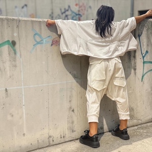 May include: An off-white oversized short-sleeve top with a wide fit and a pair of matching off-white cargo-style pants featuring large flap pockets on the thighs and cuffed hems, paired with chunky black platform sneakers.