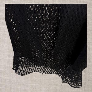 May include: Black open-weave fabric, possibly a top or shawl, with a delicate, lacy pattern. The fabric drapes softly, showcasing the intricate design. The words "NEW IN" are repeated across the top and bottom of the image.