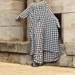 Puede incluir: Un vestido camisero a cuadros blancos y negros con mangas largas. El vestido tiene una botonadura frontal, un cuello y un dobladillo asimétrico. La modelo lleva sandalias de plataforma negras.