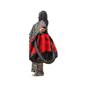 May include: A large tote bag with a red and black design. The bag has a red centre with black accents and a black base. The bag is being held by a person wearing a black and white patterned outfit.