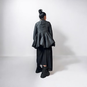 Può includere: Un top nero a maniche lunghe con volant, scollo alto e una gonna nera abbinata. L'abito è indossato da una persona con i capelli scuri raccolti in uno chignon.