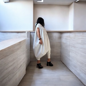 Könnte beinhalten: Eine Frau trägt ein weißes, überdimensioniertes Hemdbkleid mit leicht geraffter Taille. Sie trägt schwarze Plateausandalen und steht in einem Raum mit weißen Wänden und Holzböden.