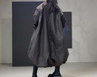 Pode incluir: Um casaco preto oversized com uma silhueta volumosa única. O casaco apresenta uma forma arredondada, semelhante a uma bolha na parte inferior, combinado com botas de plataforma pretas. A modelo está de costas, mostrando o design do casaco.