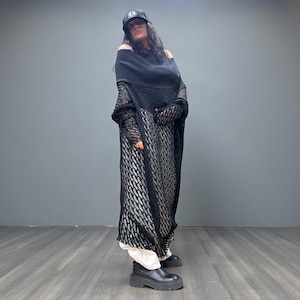 May include: A person wearing a black outfit with a black cap. The outfit includes a black off-the-shoulder top, a long black patterned dress, and black boots. The person is standing on a wooden floor.