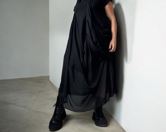 May include: A black maxi dress with a draped design and a sheer overlay. The dress is worn with black platform boots.