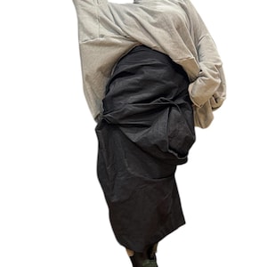 May include: A light grey oversized sweatshirt with a wide neckline and long sleeves. The model is wearing a dark grey, draped skirt and black boots with a thick sole. The outfit is casual and comfortable.
