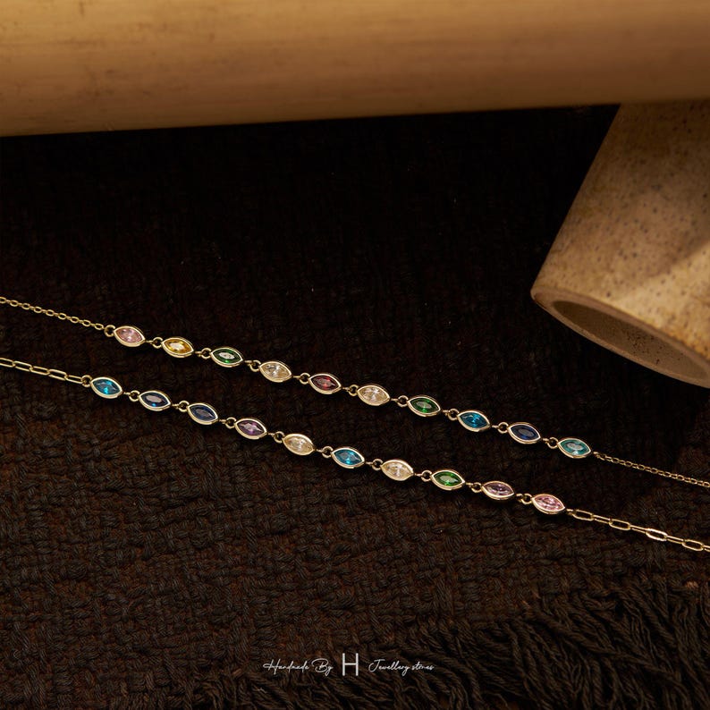 May include: Two delicate gold-tone chains featuring a series of marquise-cut multicolored gemstones. The stones are set in a repeating pattern of pink, yellow, green, blue, and clear hues. The chains include small metal links and a clasp closure.