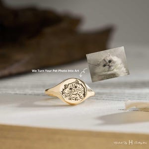 Peut inclure: Une bague chevalière dorée avec un plateau circulaire gravé d'un dessin au trait détaillé représentant un chat au pelage touffu. Le texte "We Turn Your Pet Photo Into Art" accompagne une petite photographie du chat utilisée pour la gravure.