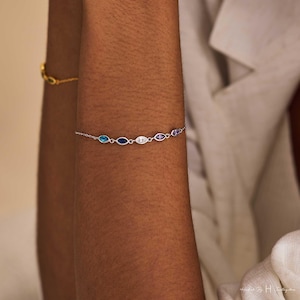 May include: A delicate silver chain bracelet featuring five marquise-cut gemstones in a row. The stones display a gradient of colors including light blue, dark blue, clear white, light purple, and a deeper purple, all set in polished silver metal links.