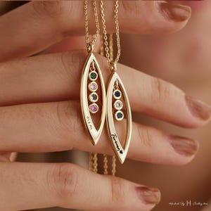 May include: Two gold necklaces with leaf-shaped pendants. One pendant has five colorful gemstones and the word "Mom" engraved on it. The other pendant has five clear gemstones and the word "Forever" engraved on it.