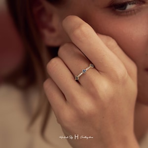 May include: A gold ring featuring a thin band set with small clear stones and three evenly spaced dark blue four-leaf clover motifs. The ring is positioned on a finger, and the text "Handmade By H Jewellery stones" is visible at the bottom.