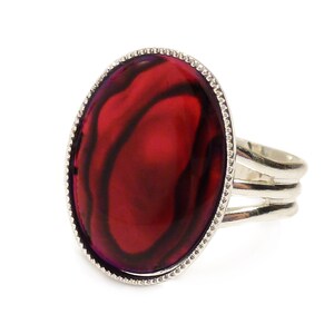 May include: A silver ring featuring a large oval red gemstone set in a silver bezel. The ring has a triple band design.