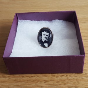Op de afbeelding: Een zilveren ring met een ovale cameo met een zwart-wit portret van Edgar Allan Poe.