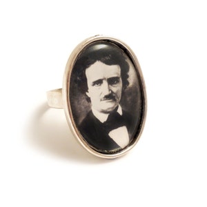 Op de afbeelding: Een zilveren ring met een ovale cameo met een zwart-wit portret van Edgar Allan Poe.