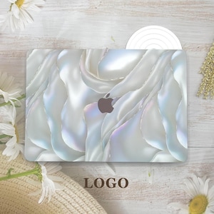 May include: A white laptop case with a pearlescent, flowing design. The case features a subtle, iridescent sheen and a dark gray Apple logo. The word "LOGO" is printed in brown at the bottom of the case.