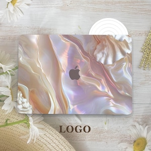 May include: A laptop computer with a white and pink iridescent shell-like design. The Apple logo is visible on the laptop.