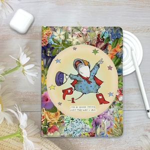 May include: A decorative journal with a floral pattern and a cartoon mouse illustration. The mouse is wearing a cape and boots, with the text "I'M A GOOD THING JUST THE WAY I AM". The journal is surrounded by flowers.