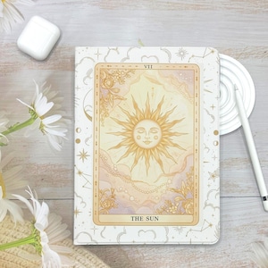 May include: A white and gold tarot card-themed tablet case featuring "The Sun" card design. The case has a celestial pattern with clouds, stars, and moons. A white stylus, a white wireless earbud case, and a white coaster are also visible.