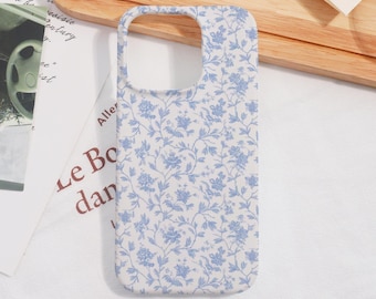 May include: A phone case with a floral pattern. The case is white with a repeating design of blue flowers and leaves. The case has cutouts for the camera and buttons.
