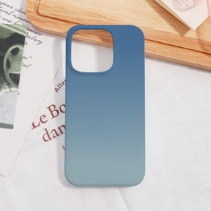 May include: A blue ombre phone case with a gradient effect, transitioning from a darker blue at the top to a lighter blue at the bottom. The case has a cutout for the camera and flash.
